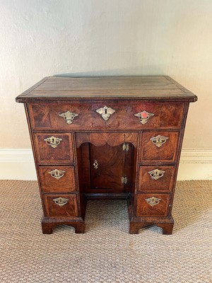Lot 1055 - George II walnut and crossbanded and featherbanded kneehole desk, the top with re-entrant angles, having seven drawers and shaped frieze drawer about the cupboard kneehole on bracket feet, 69cm wid...
