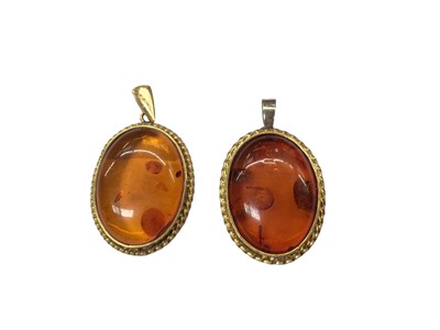 Lot 1060 - Two 18ct gold mounted oval amber pendants