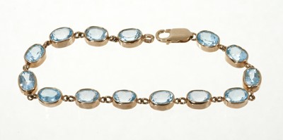 Lot 357 - Blue topaz and gold bracelet with 14 oval mixed cut blue topaz in 9ct gold setting, 19.5cm.