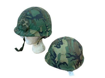 Lot 784 - American M1 steel helmet complete with liner, chinstrap and camouflage cover, together with another American M1 steel helmet, also with a camouflage cover (2)