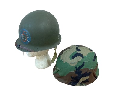 Lot 785 - American M1 steel helmet complete with liner, chinstrap and camouflage cover, together with another American M1 steel helmet, named on the reverse to SGT. Finnly (2)