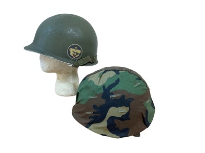 Lot 786 - American M1 steel helmet complete with liner, chinstrap and camouflage cover, together with another American M1 steel helmet, also with a camouflage cover (2)