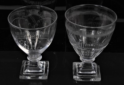 Lot 303 - Two George III wine glasses, one with etched initials and swags, the other with cut and etched decoration, both on pyramid base with square foot (2).