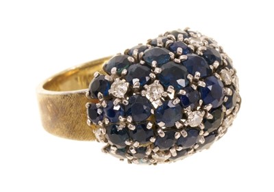 Lot 668 - 1960s sapphire and diamond cluster ring with a bombé cluster of pavé-set round mixed cut blue sapphires and brilliant cut diamonds in claw setting on a textured 14k gold tapered shank.