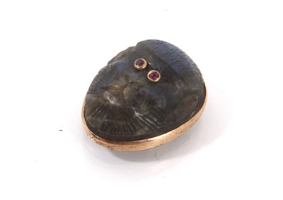 Lot 856 - Unusual 19th century carved labradorite cabochon in the form of a monkey's face, with ruby eyes and gold mounts, 18.4 x 14.6mm.