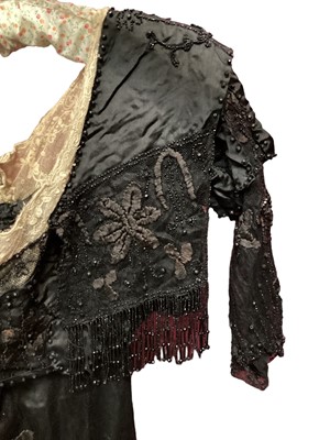 Lot 2104 - Edwardian evening dress in black satin with beaded net overlay, high waist and asymmetric draping and fringing.