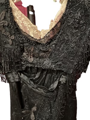 Lot 2104 - Edwardian evening dress in black satin with beaded net overlay, high waist and asymmetric draping and fringing.