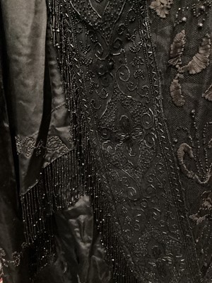 Lot 2104 - Edwardian evening dress in black satin with beaded net overlay, high waist and asymmetric draping and fringing.