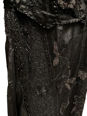 Lot 2104 - Edwardian evening dress in black satin with beaded net overlay, high waist and asymmetric draping and fringing.
