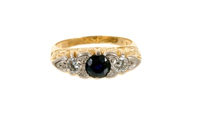 Lot 500 - Victorian style sapphire and diamond three stone ring with a round mixed cut blue sapphire flanked by two brilliant cut diamonds in carved gold setting on 18ct gold shank