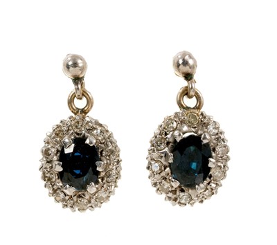 Lot 501 - Pair of sapphire and diamond cluster earrings with an oval mixed cut blue sapphire surrounded by a border of single cut diamonds.