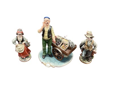 Lot 1270 - Capodimonte porcelain figure of a fruit seller with market stall, together with a pair of Capodimonte figures (3)