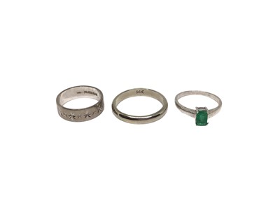 Lot 135 - 18ct white gold wedding ring, white metal wedding ring (stamped 14K) and one other white metal emerald single stone ring (3)