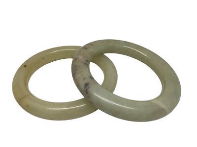 Lot 210 - Two jade/ green hard stone polished round bangles, 9.5cm diameter