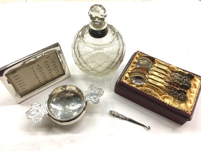 Lot 1099 - Silver framed desk calendar, tea strainer stamped 'sterling', set of six silver (835) coffee spoons with rose decoration, silver handled button hook and a silver collared glass scent bottle