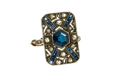 Lot 454 - Art Deco sapphire and diamond cocktail ring with a rectangular openwork plaque centred with a hexagonal cut blue sapphire, calibre cut blue sapphires and rose cut diamonds in millegrain setting, pi...