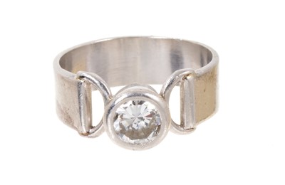 Lot 565 - 1970s diamond single stone ring with a round brilliant cut diamond estimated to weigh approximately 1.06cts in rub over setting with stylized shoulders on wide platinum band, accompanied by an Insu...