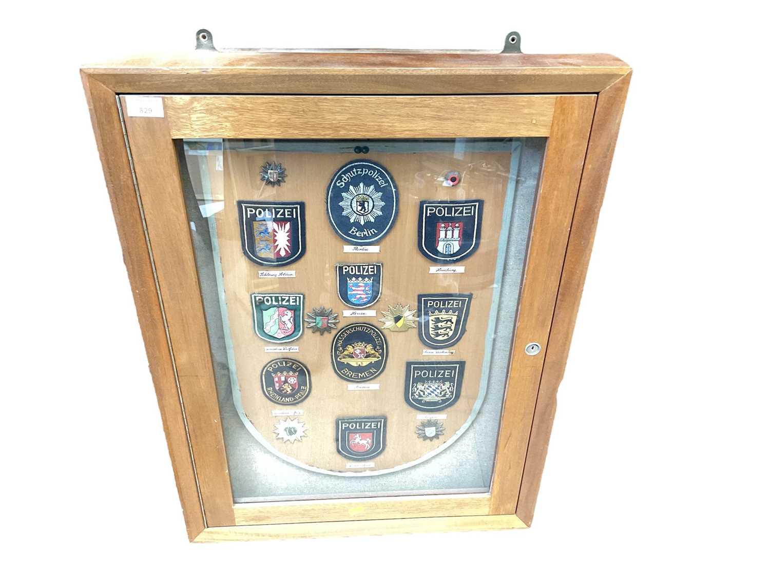 Lot 829 - Glazed wall mounted cabinet containing a display of German Police badges.