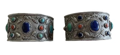 Lot 585 - Pair of Chinese silver and gem set cuff bangles, each with a lapis lazuli, turquoise and coral cabochons on floral repoussé silver ground.