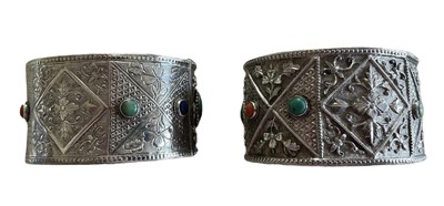 Lot 585 - Pair of Chinese silver and gem set cuff bangles, each with a lapis lazuli, turquoise and coral cabochons on floral repoussé silver ground.