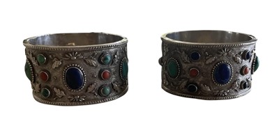 Lot 585 - Pair of Chinese silver and gem set cuff bangles, each with a lapis lazuli, turquoise and coral cabochons on floral repoussé silver ground.