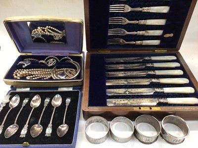 Lot 1092 - Four silver napkin rings, jewellery, plated souvenir spoons and a mother of pearl handled plated knife and fork set in wooden case