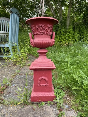 Lot 1222 - Set of three small cast iron urns, red painted, raised on pedestal bases, 72cm high