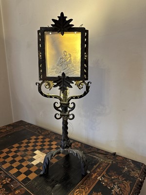 Lot 1617 - Wrought iron standard lamp, with acanthus ornament on four leaf clad supports, with shade, and a similar smaller lamp with porcelain panel shade depicting figures. (2)