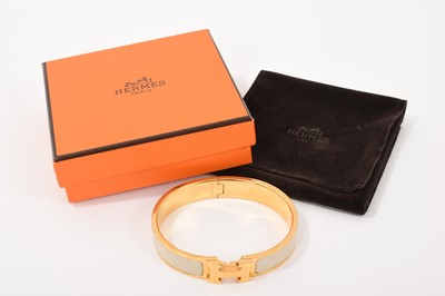 Lot 570 - Hermès bangle, the gilt bangle with signature logo 'H' clasp and cream enamel band, signed. In original Hermès pouch and box.