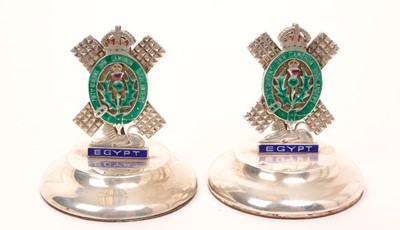 Lot 427 - A pair of sterling silver and enamel regimental menu holders for the 79th Queen's Own Cameron Highlanders, on circular silver bases, marked 'Sterling Silver' 6.5cm high.