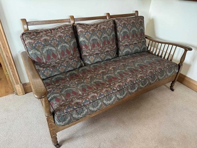 Lot 1614 - Arts and Crafts oak three seater settee with Liberty fabric on spindle supports raised on castors. 178cm wide