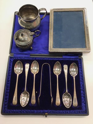 Lot 1043 - Cased set of six silver teaspoons and pair of silver sugar tongs, silver photograph frame, Georgian silver milk jug, silver mustard pot and group of plated ware