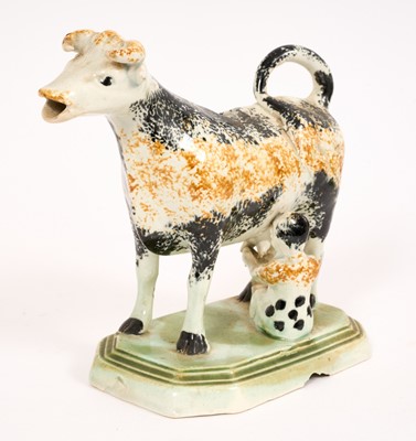 Lot 281 - Pearlware cow creamer, circa 1820, with black and ochre sponged decoration, on green stepped base with milkmaid, 14cm high