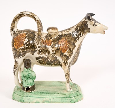 Lot 283 - Prattware cow creamer, circa 1820, with ochre and brown decoration, on a green stepped base with milkmaid, 14.5cm high