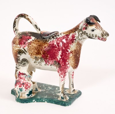 Lot 284 - Pearlware cow creamer, circa 1820, with pink, brown and black sponged decoration, on a green sponged base with milkmaid, 13.5cm high