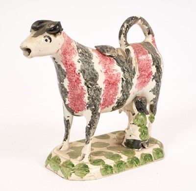 Lot 285 - Pearlware cow creamer, circa 1820, with sponged pink and black stripe decoration, on a green sponged base with milkmaid, 14cm high