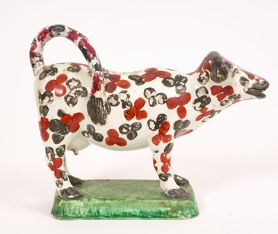 Lot 287 - Pearlware cow creamer, circa 1820, with enamelled flower head decoration, on a green base, 12.6cm high