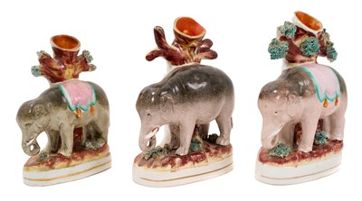 Lot 297 - Three Victorian Staffordshire elephant spill vases, all modelled standing in front of trees, on gilt-lined bases, 14.5cm to 17cm high