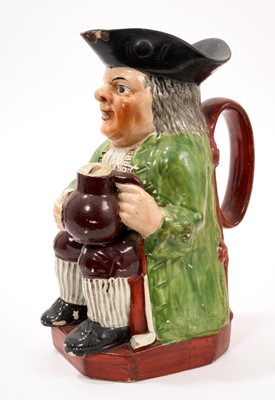 Lot 304 - Early 19th century pearlware glazed Toby jug, wearing a green jacket, check shirt, maroon and striped breeches, on a red base, 24cm high