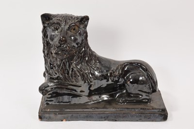 Lot 310 - 19th century treacle glazed figure of a recumbent lion, modelled with naive facial features, on a stepped rectangular base, 28cm wide