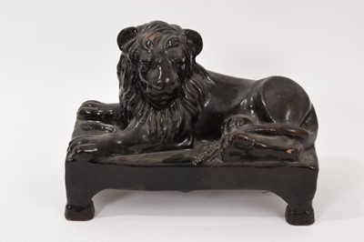 Lot 311 - 19th century treacle glazed pottery figure of a recumbent lion, on a rectangular base with four legs, 26.5cm wide