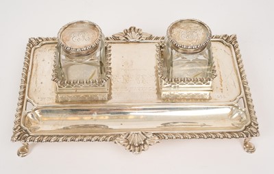 Lot 527 - Victorian silver inkstand of rectangular form with engraved presentation inscription, two removable cut glass ink bottles with silver mounts, gadrooned and shell borders, raised on four hoof fee...