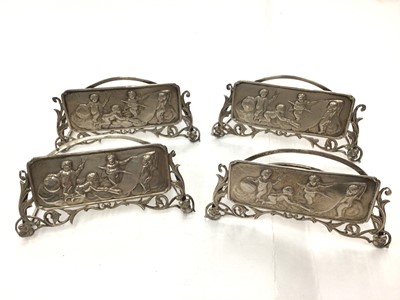 Lot 35 - Set of four Edwardian silver menu holders, each rectangular plaque decorated with putti writing on a paper scroll with pierced floral scroll borders (London 1907)