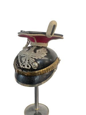 Lot 826 - Imperial German Uhlan NCO's Lance cap with black leather body, red and white piped cloth top, silvered eagle helmet plate , gilt brass chin scales and original black leather liner, Provenance...