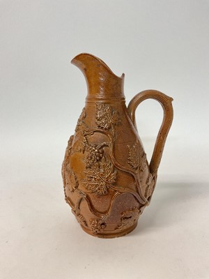 Lot 111 - 19th century relief moulded pottery jug decorated with vines and grapes and a figure seated on a barrel, initialled GB to base, 23cm high