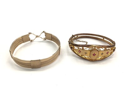 Lot 1109 - Gilt metal bangle with a central yellow metal plaque mounted with two old cut diamonds and three rubies, together with one other gilt metal bangle (2)