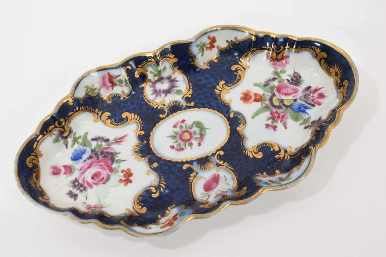 Lot 37 - A Worcester lobed hexagonal form spoon tray, circa 1768, painted with panels of flower sprays within gilt scrolled borders, reserved on a blue scale ground, square mark, 15cm wide