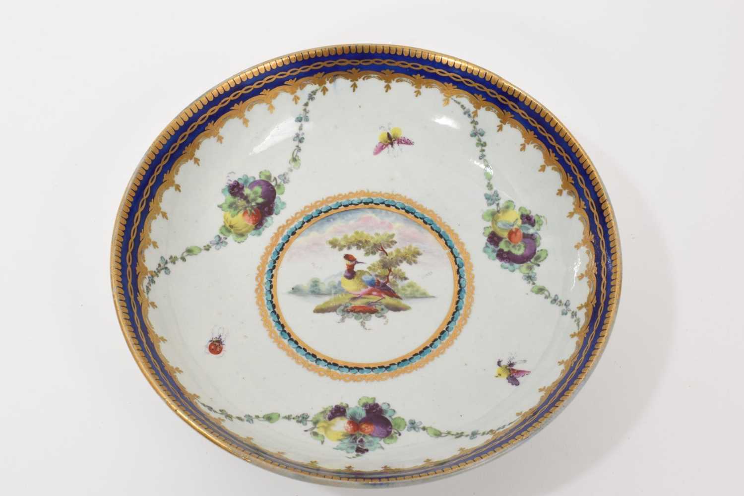 Lot 34 - A Worcester 'Lord Rodney' type saucer dish, circa 1770, painted with a colourful bird, swags of fruit and insects, with gilded blue edges, 16cm diameter