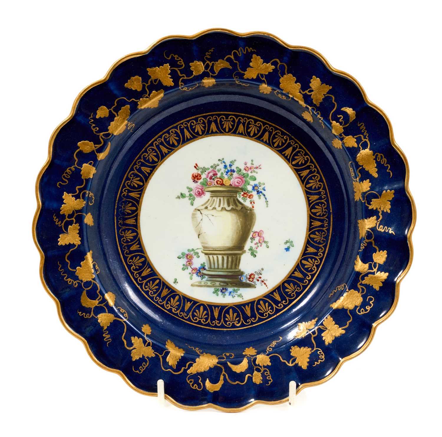 Lot 45 - A Worcester scalloped dessert plate, circa 1770, decorated in the workshop of James Giles, painted in the centre with a classical urn, draped in garlands of pink coloured flowers, rich gilt bord...