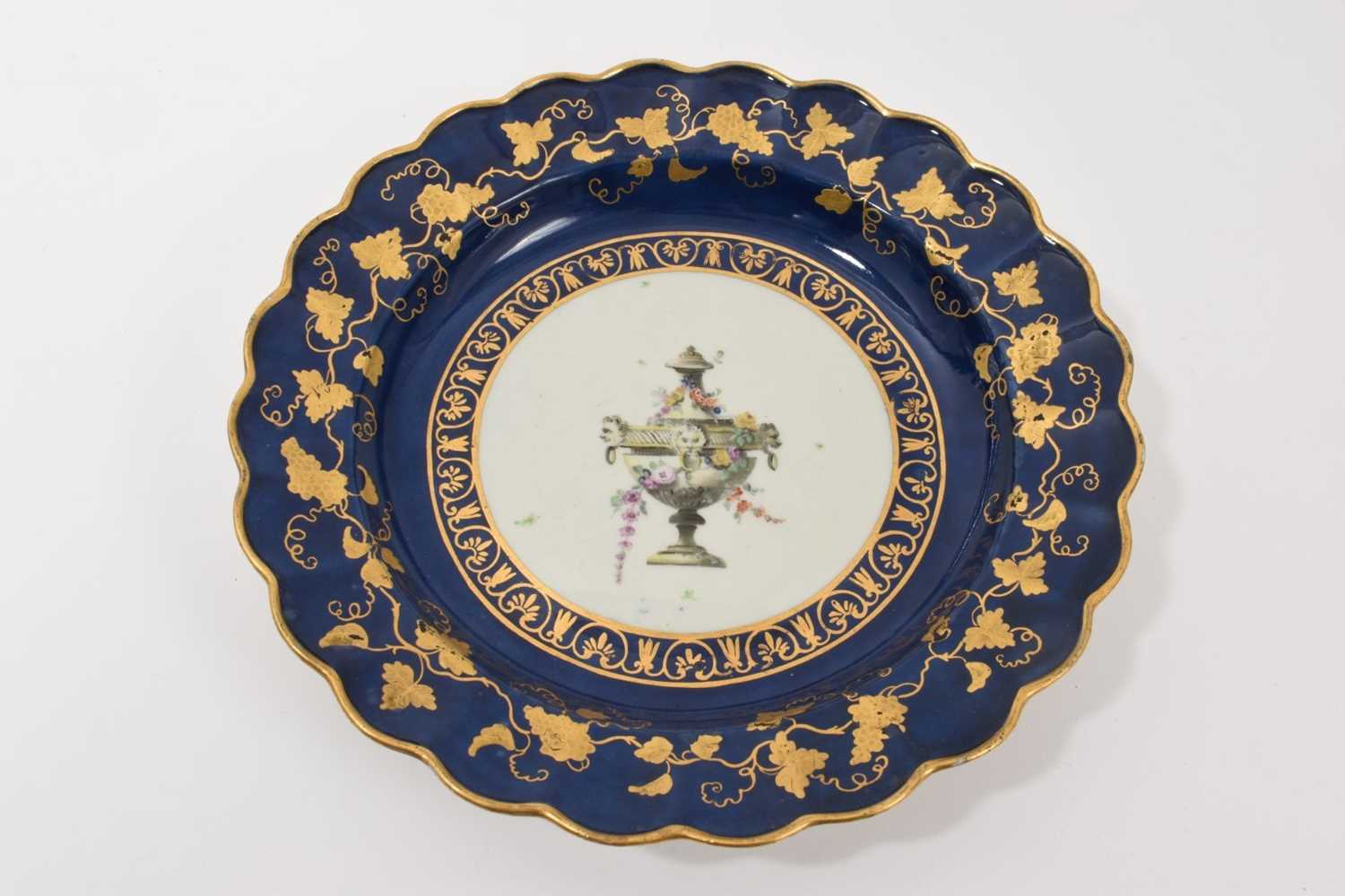 Lot 46 - A Worcester scalloped dessert plate, circa 1770, decorated in the workshop of James Giles, painted in the centre with a classical urn, draped in garlands of pink coloured flowers, rich gilt bord...